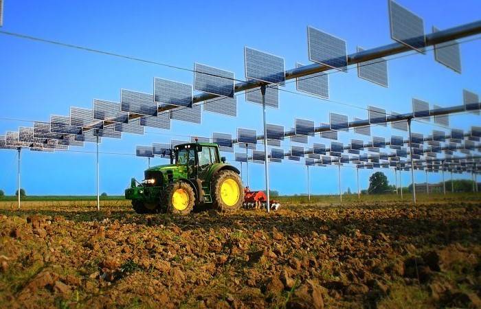 Dettaglio dei pannelli di un impianto agrivoltaico con macchinari agricoli al lavoro sotto.